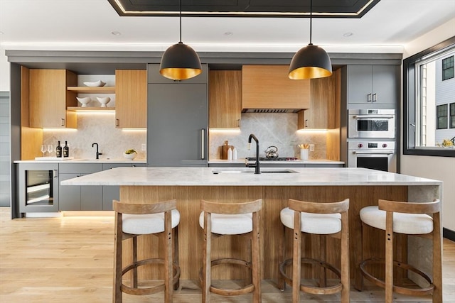 kitchen with light stone counters, sink, decorative light fixtures, and a center island with sink