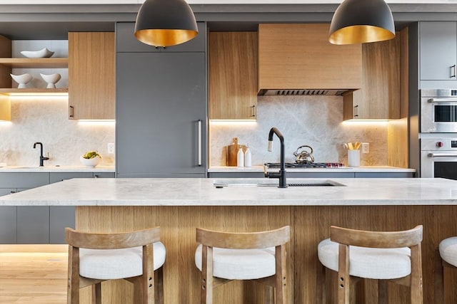 kitchen featuring sink, custom exhaust hood, a breakfast bar area, light stone countertops, and decorative backsplash