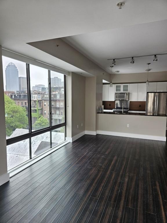 unfurnished living room with dark wood-style floors, rail lighting, a city view, a wall of windows, and baseboards