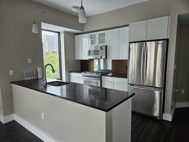 kitchen with appliances with stainless steel finishes, a sink, dark countertops, a peninsula, and dark wood-style floors