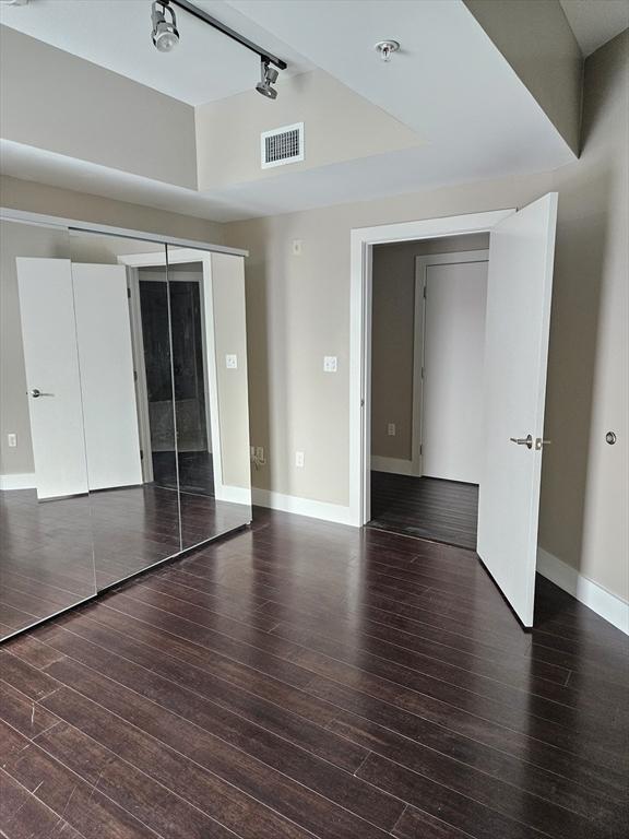 unfurnished bedroom with wood-type flooring, rail lighting, baseboards, a tray ceiling, and a closet