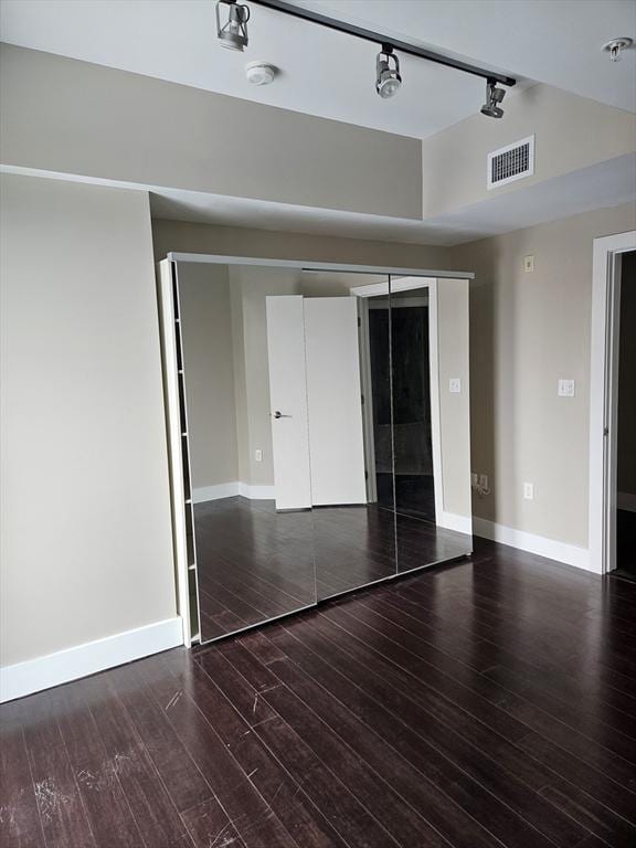 unfurnished bedroom featuring track lighting, baseboards, wood finished floors, and a closet