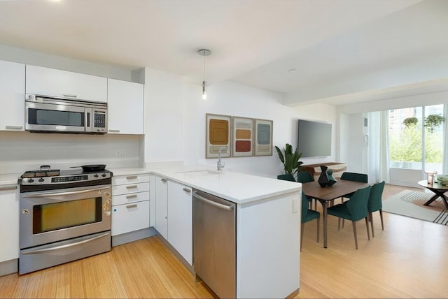 kitchen featuring appliances with stainless steel finishes, a sink, a peninsula, and light countertops