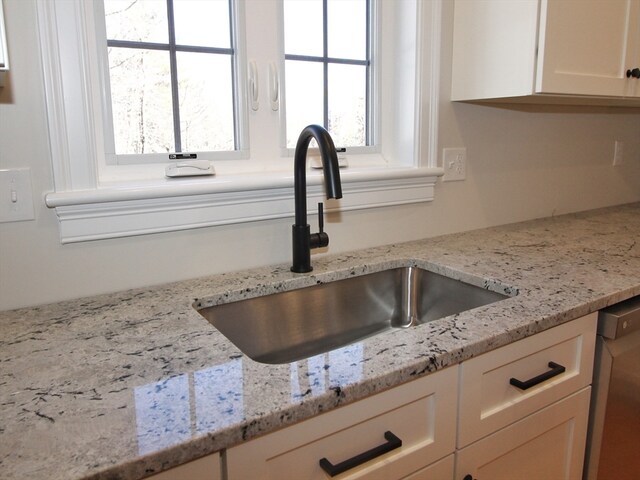 room details featuring white cabinets, dishwasher, light stone countertops, and sink