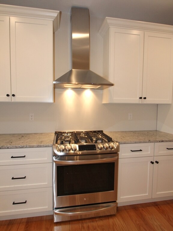 kitchen with wall chimney range hood, gas range, light wood-type flooring, and white cabinetry