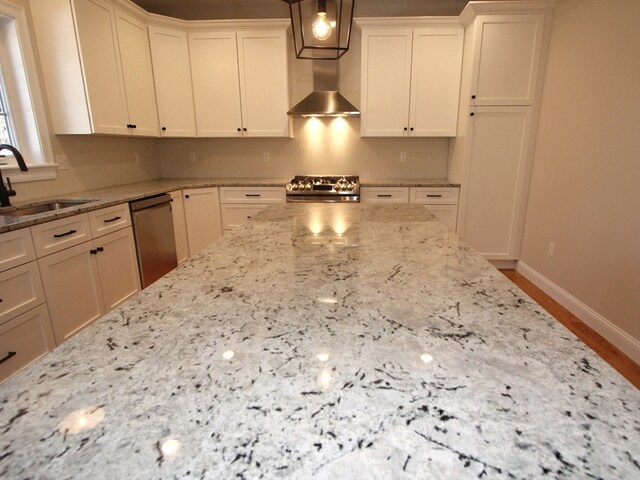 kitchen with wall chimney exhaust hood, decorative light fixtures, sink, white cabinets, and appliances with stainless steel finishes