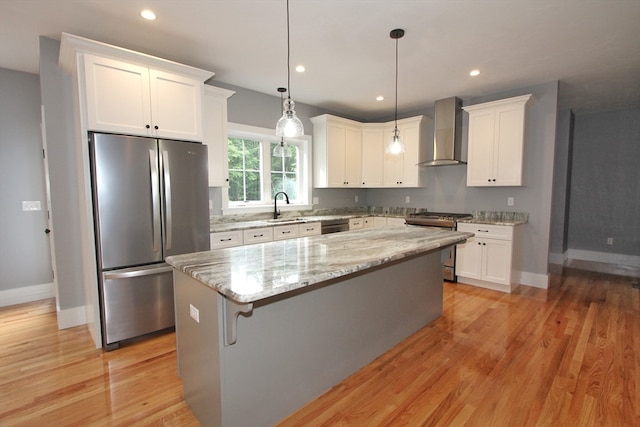 kitchen featuring light wood-type flooring, stainless steel appliances, wall chimney exhaust hood, and white cabinetry