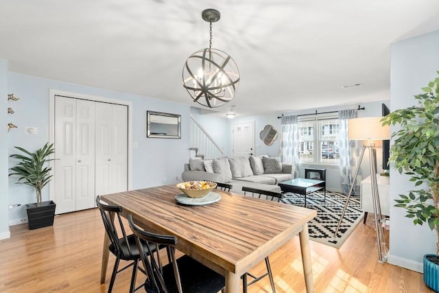 dining space with baseboards, light wood finished floors, a chandelier, and stairway