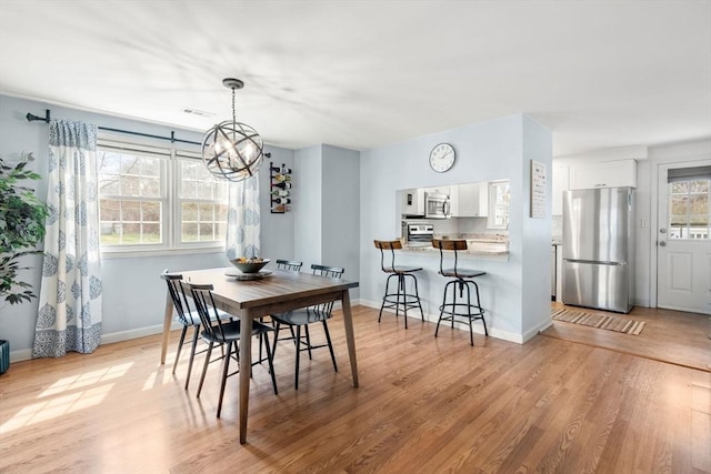 dining area with baseboards, a notable chandelier, and light wood-type flooring