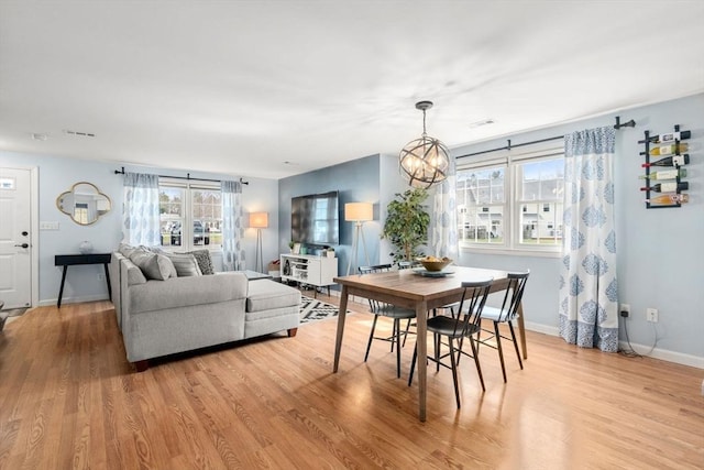 dining room with light wood-style floors, baseboards, a notable chandelier, and a wealth of natural light