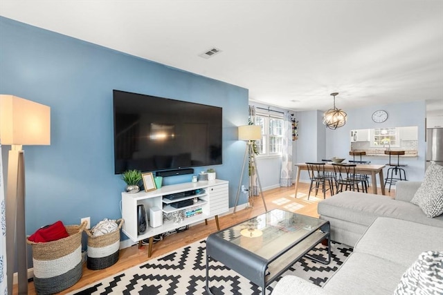 living area with an inviting chandelier, baseboards, wood finished floors, and visible vents