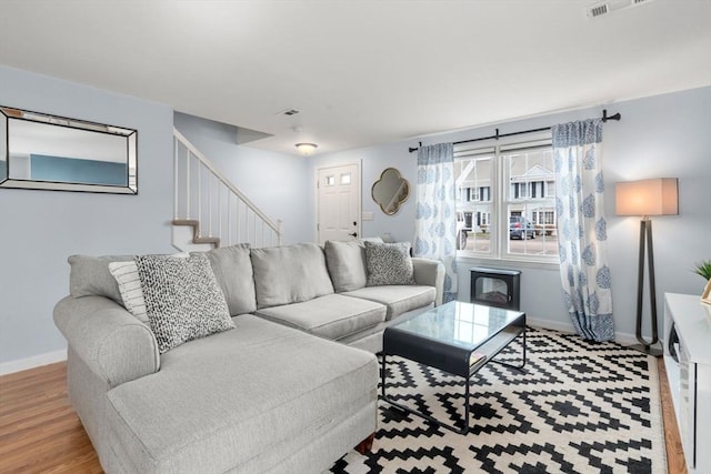 living room with stairs, baseboards, visible vents, and wood finished floors