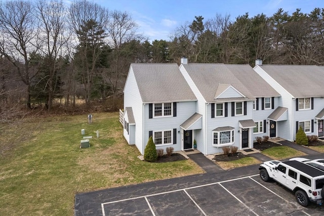view of front facade with roof with shingles, a chimney, uncovered parking, and a front yard