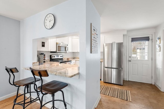 kitchen with decorative backsplash, a breakfast bar area, light stone counters, white cabinets, and stainless steel appliances