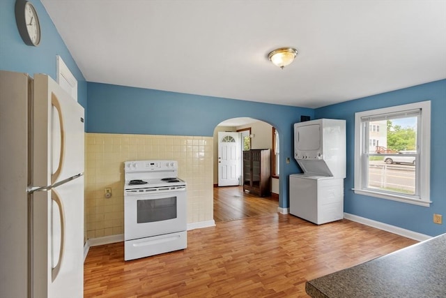 16 Elm St, Leominster, MA 01453 - kitchen featuring white appliances, stacked washer and clothes dryer, arched walkways, light wood-style flooring, and tile walls