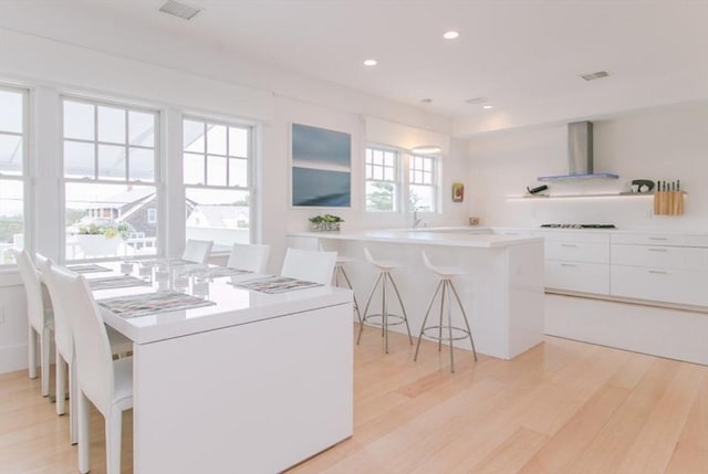 kitchen with visible vents, wall chimney exhaust hood, modern cabinets, and a kitchen bar
