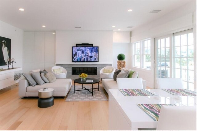 living area featuring recessed lighting, a glass covered fireplace, and light wood finished floors