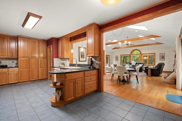 kitchen with tile patterned flooring, a sink, backsplash, brown cabinetry, and a chandelier