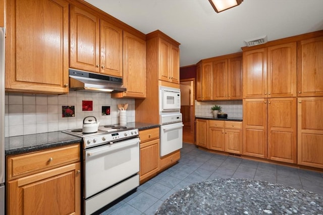 kitchen featuring white appliances, under cabinet range hood, backsplash, tile patterned floors, and brown cabinetry