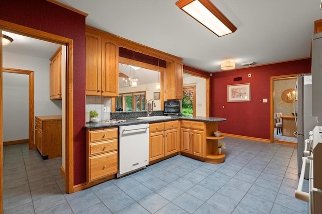kitchen featuring white dishwasher, a sink, light tile patterned floors, and dark countertops
