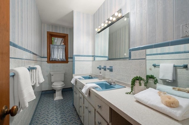 bathroom with toilet, wainscoting, vanity, wallpapered walls, and tile walls