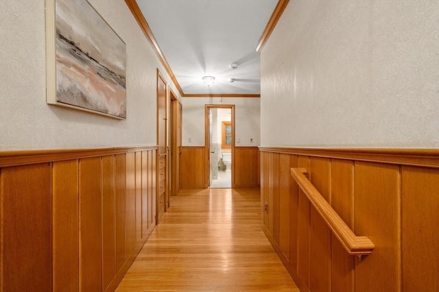hall with wainscoting, light wood-style floors, crown molding, and wooden walls