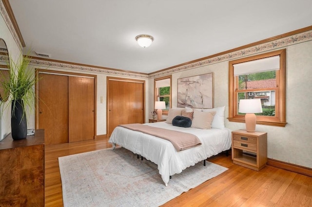 bedroom with light wood-style flooring, multiple closets, crown molding, and baseboards