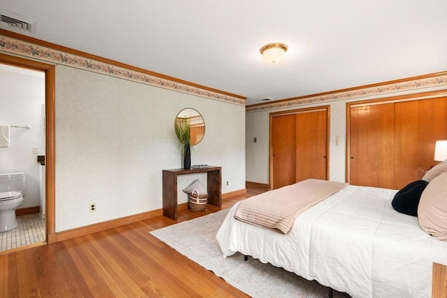bedroom featuring wood finished floors, multiple closets, connected bathroom, crown molding, and baseboards