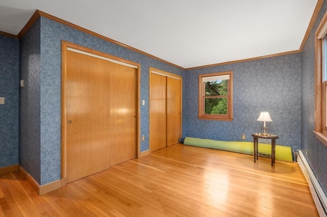 unfurnished bedroom with wood finished floors, a baseboard heating unit, crown molding, two closets, and wallpapered walls