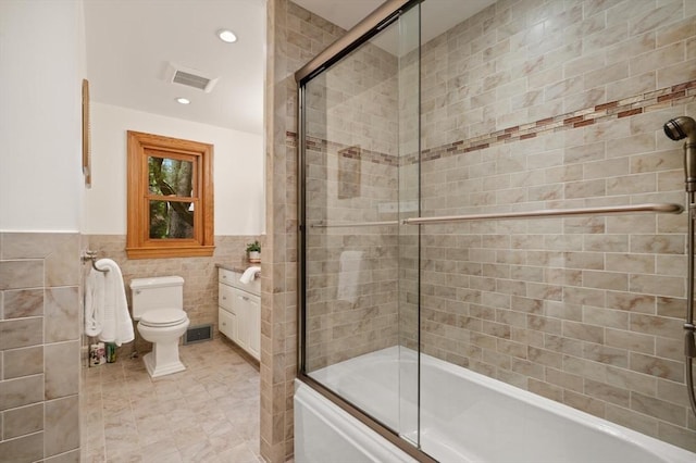bathroom with tile walls, bath / shower combo with glass door, toilet, recessed lighting, and wainscoting