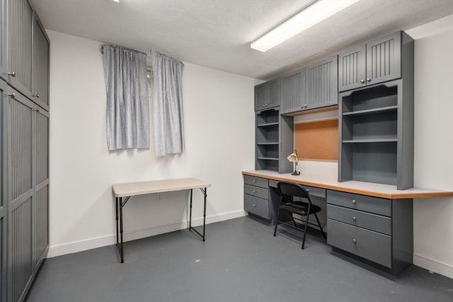 office area featuring built in study area, baseboards, and finished concrete flooring
