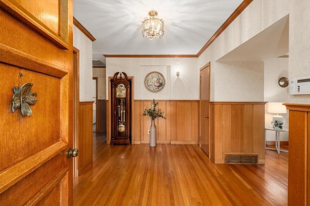 hallway featuring wood finished floors, crown molding, a chandelier, and a wainscoted wall