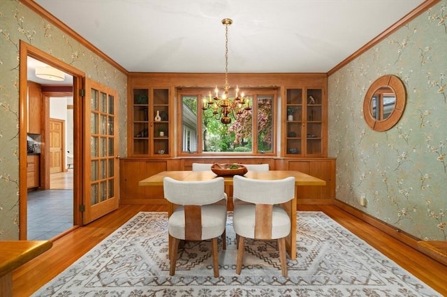 dining room with a chandelier, wood finished floors, crown molding, wallpapered walls, and baseboards