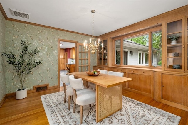 dining room featuring wallpapered walls, a chandelier, light wood finished floors, ornamental molding, and baseboards