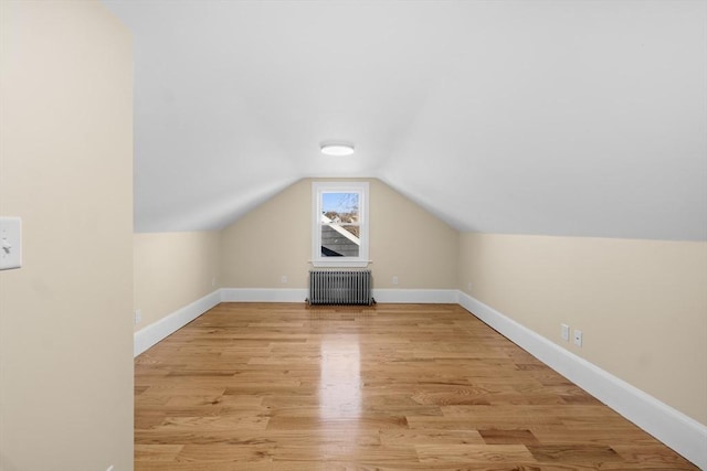 bonus room featuring radiator, light wood-style flooring, vaulted ceiling, and baseboards