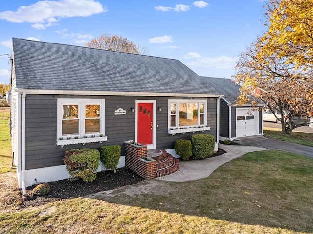 cape cod-style house with roof with shingles, asphalt driveway, an attached garage, and a front yard