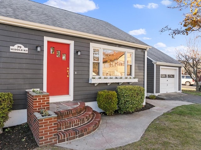 view of exterior entry with driveway, a garage, and a shingled roof