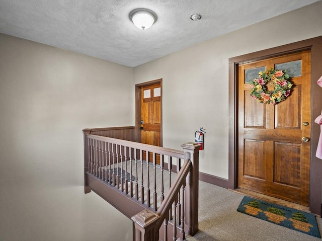 interior space with carpet, baseboards, a textured ceiling, and an upstairs landing