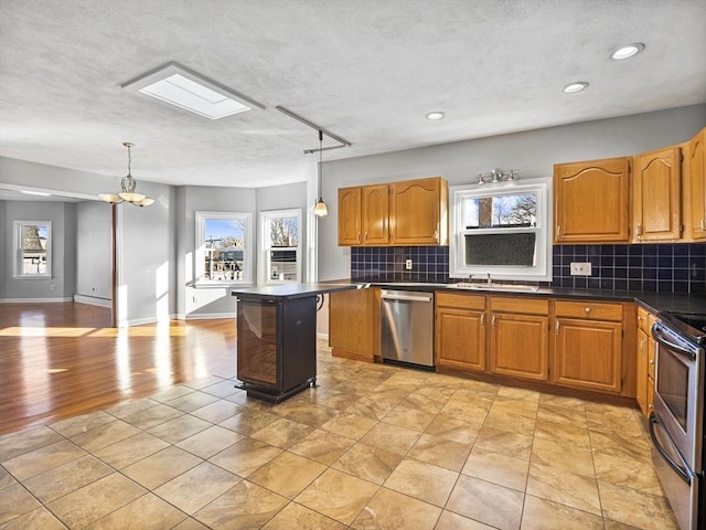 kitchen with brown cabinets, stainless steel appliances, dark countertops, tasteful backsplash, and a sink