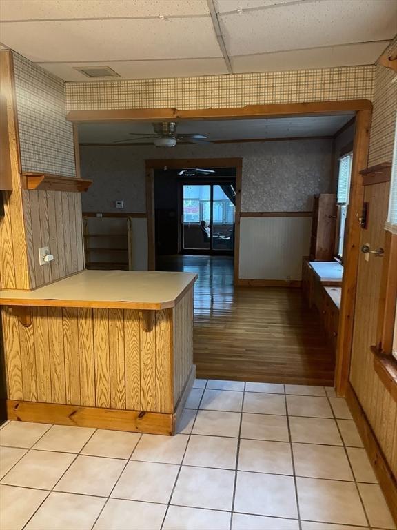 kitchen with ceiling fan, a drop ceiling, kitchen peninsula, and light tile patterned flooring