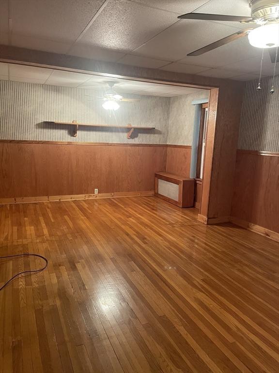 basement featuring ceiling fan, a drop ceiling, wood-type flooring, and wood walls