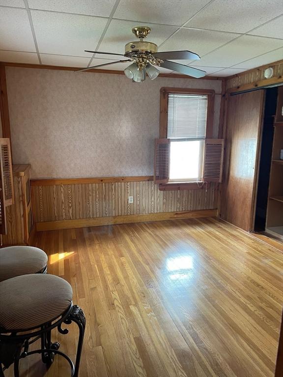 spare room with light wood-type flooring, ceiling fan, wooden walls, and a drop ceiling