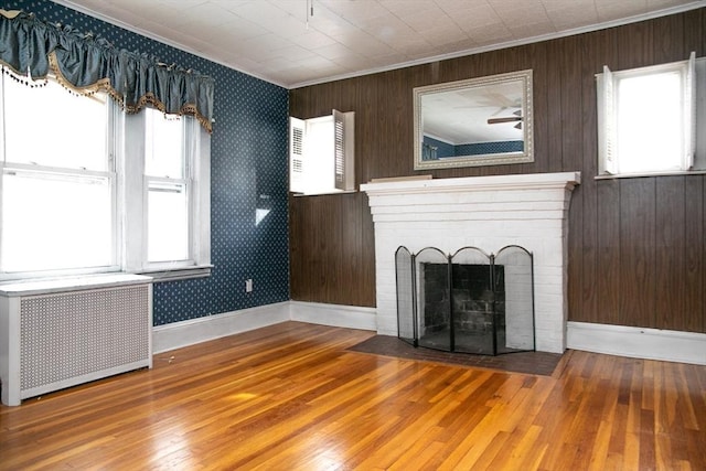 unfurnished living room with crown molding, radiator heating unit, hardwood / wood-style floors, and a brick fireplace