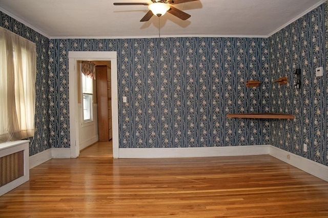 empty room with hardwood / wood-style flooring, radiator heating unit, crown molding, and ceiling fan