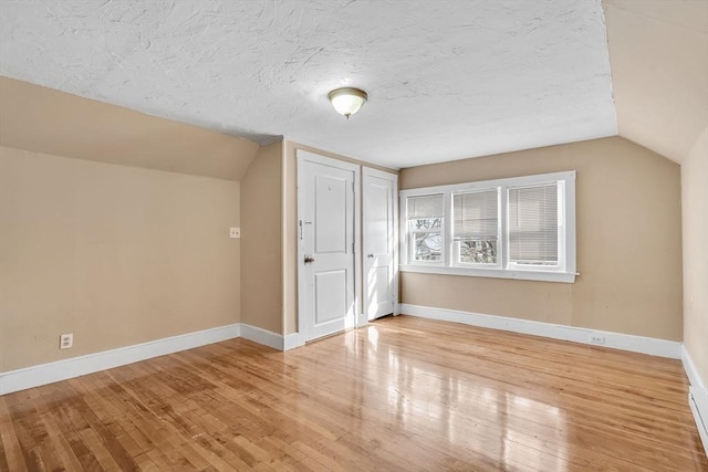 additional living space with wood-type flooring, a textured ceiling, and vaulted ceiling