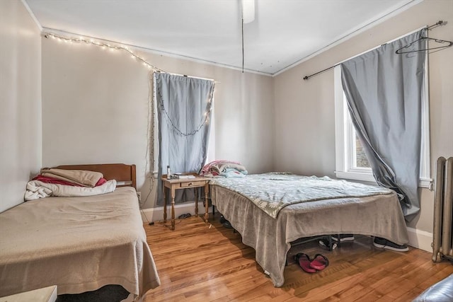 bedroom featuring ornamental molding, radiator heating unit, and light hardwood / wood-style flooring