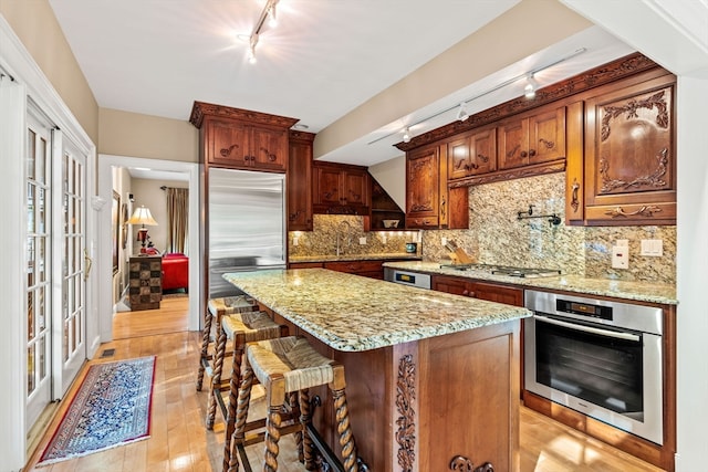 kitchen with a kitchen island, track lighting, appliances with stainless steel finishes, and light hardwood / wood-style floors