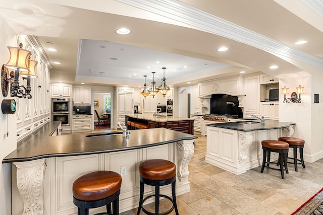 kitchen with a large island with sink, sink, a kitchen bar, pendant lighting, and a raised ceiling