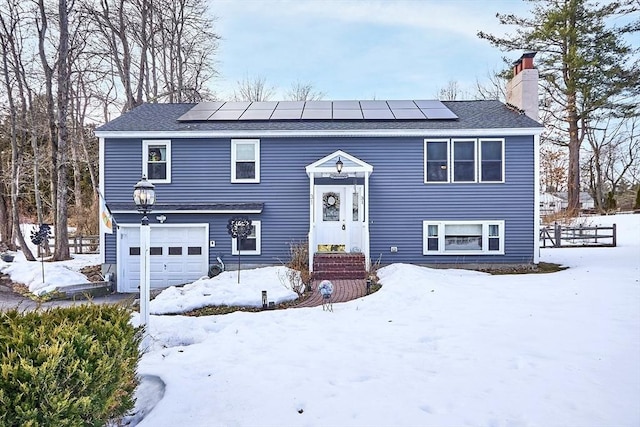 raised ranch featuring an attached garage, a chimney, and solar panels