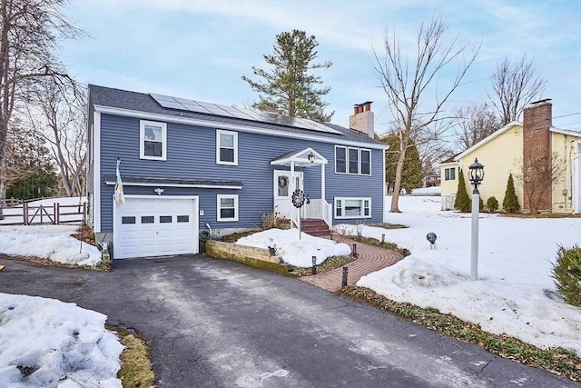 raised ranch with a garage, fence, driveway, roof mounted solar panels, and a chimney